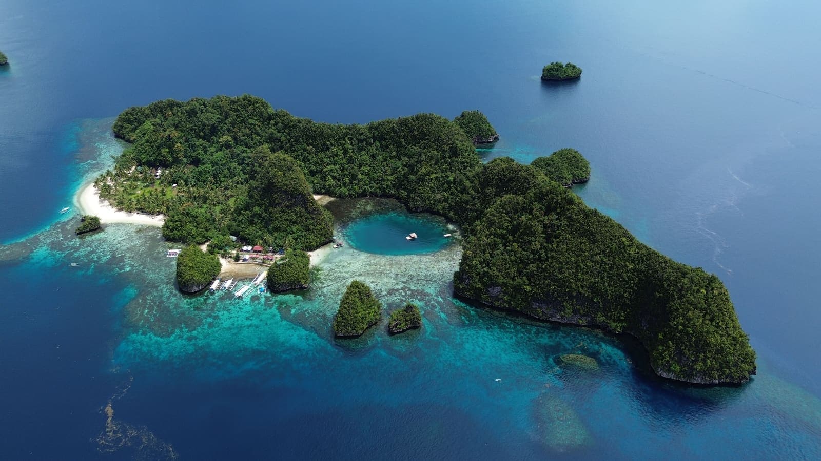 Aerial view of a forested island in Libjo ringed by shallow turquoise reef, with a white sand spit on its northern shore