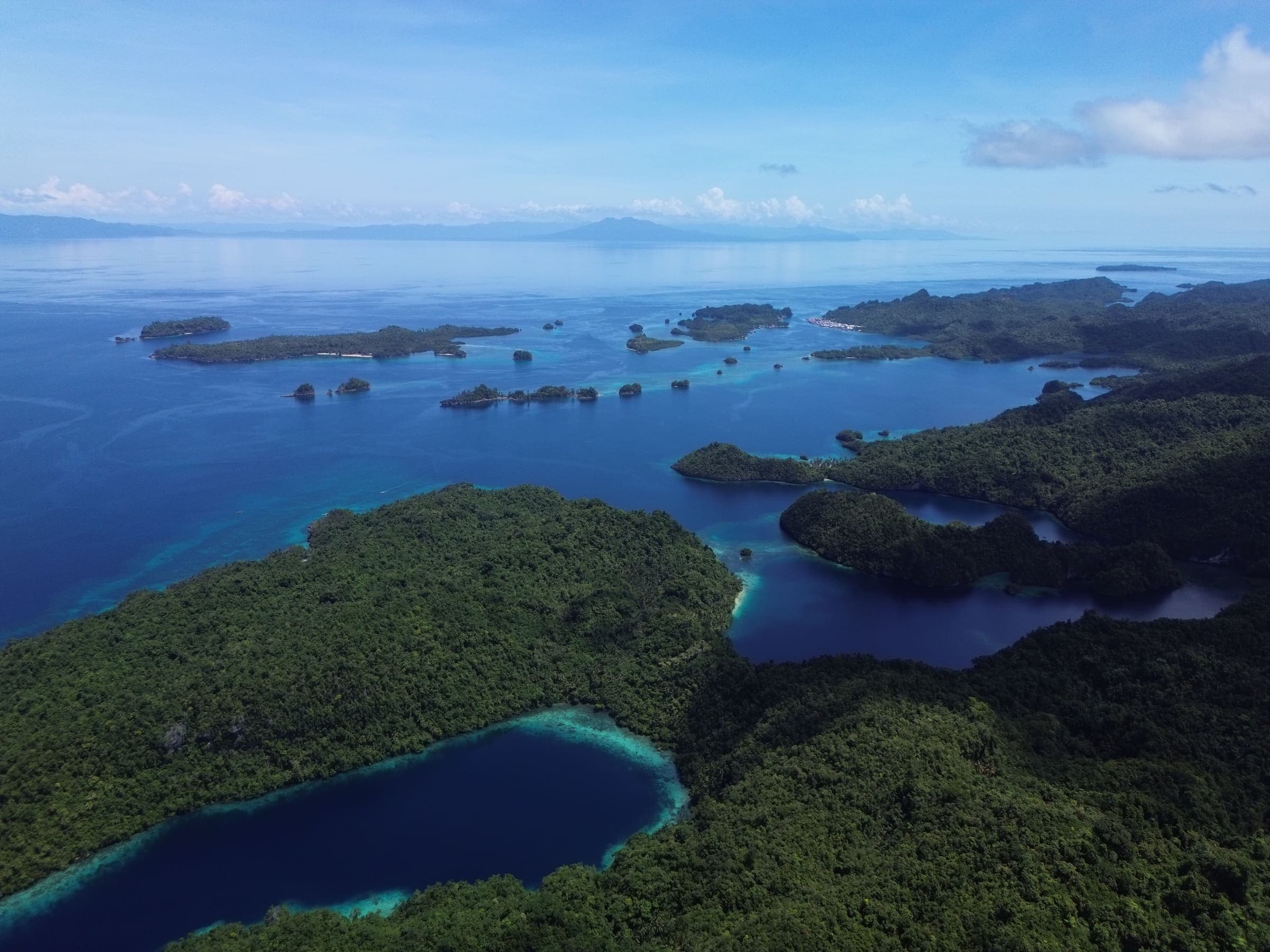 Aerial view across the Dinagat archipelago, forested islands scattered over deep blue water with the horizon beyond