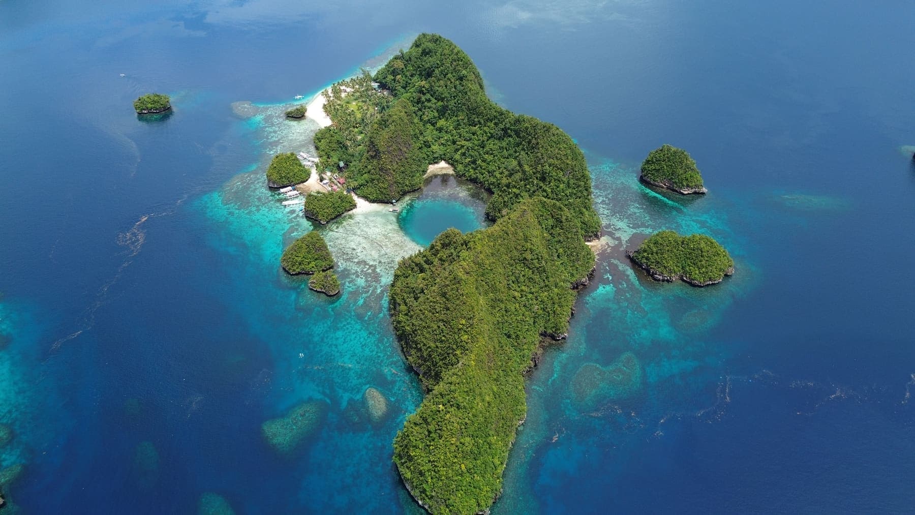 Aerial view of a forested island in Libjo surrounded by pale turquoise reef and deep blue channels